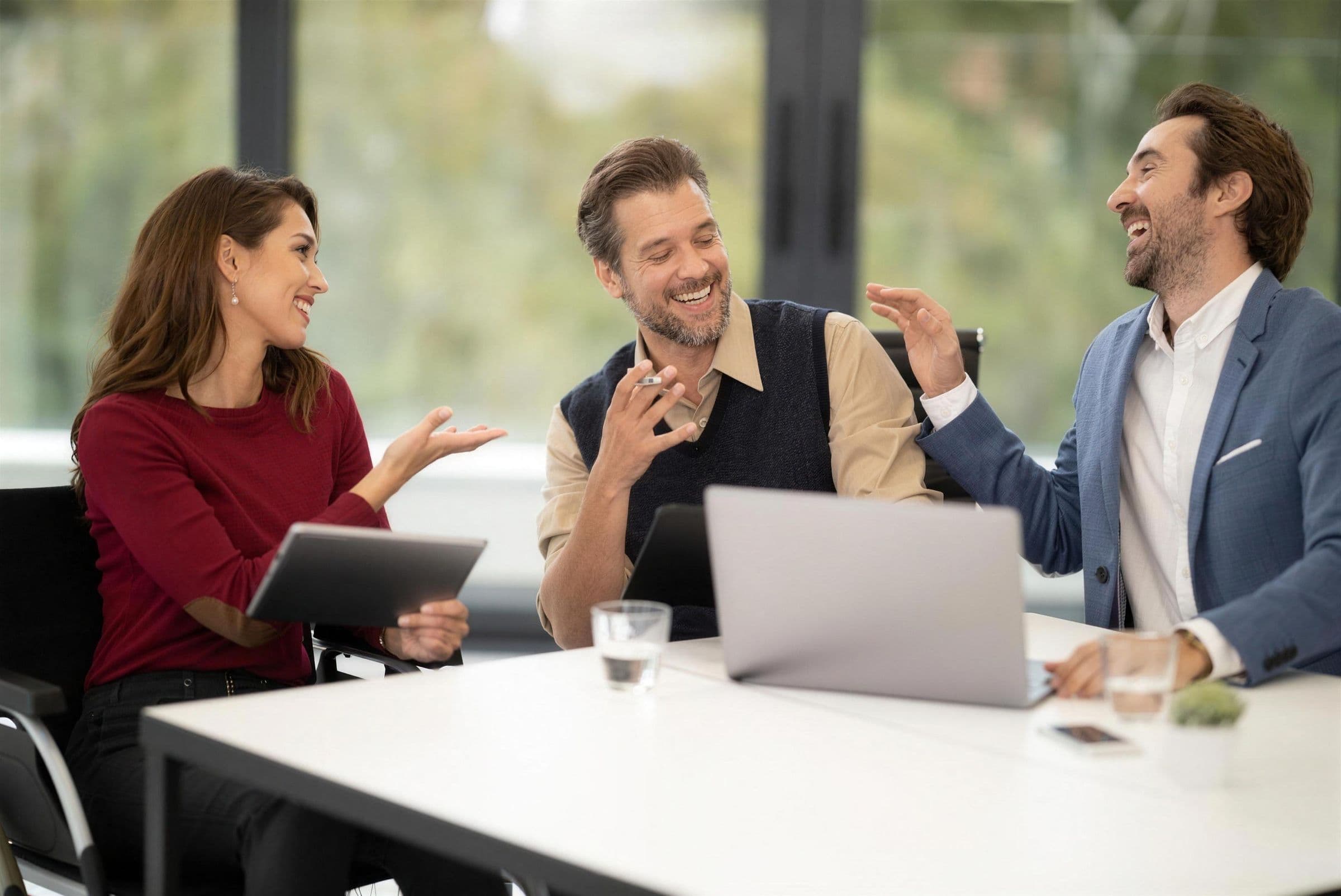 Three colleagues laughing as they go through results on a laptop at a meeting table